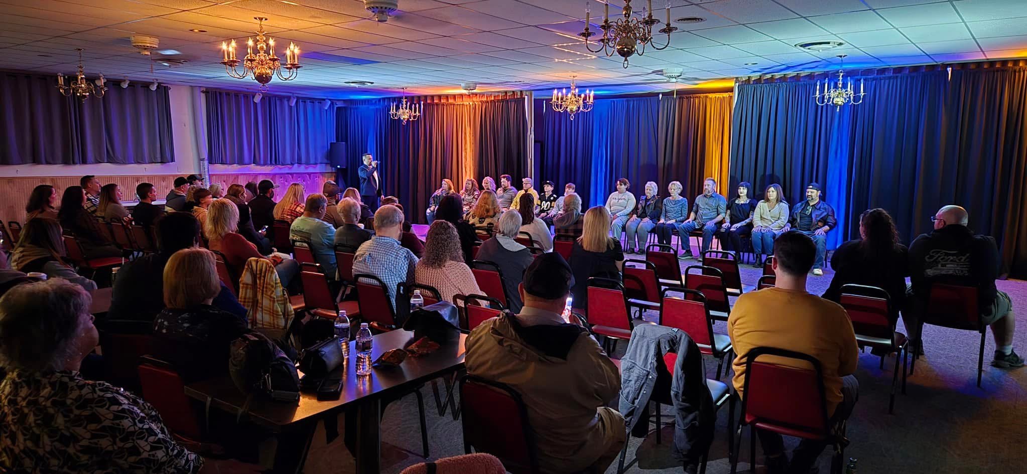 A full room watches Joe Hussey on stage with a row of hypnotized volunteers