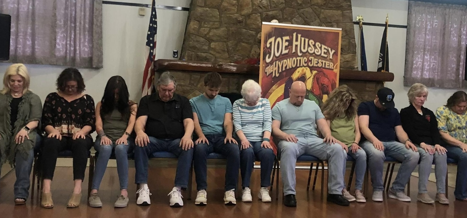 A row of volunteers in hypnosis in front of The Hypnotic Jester banner