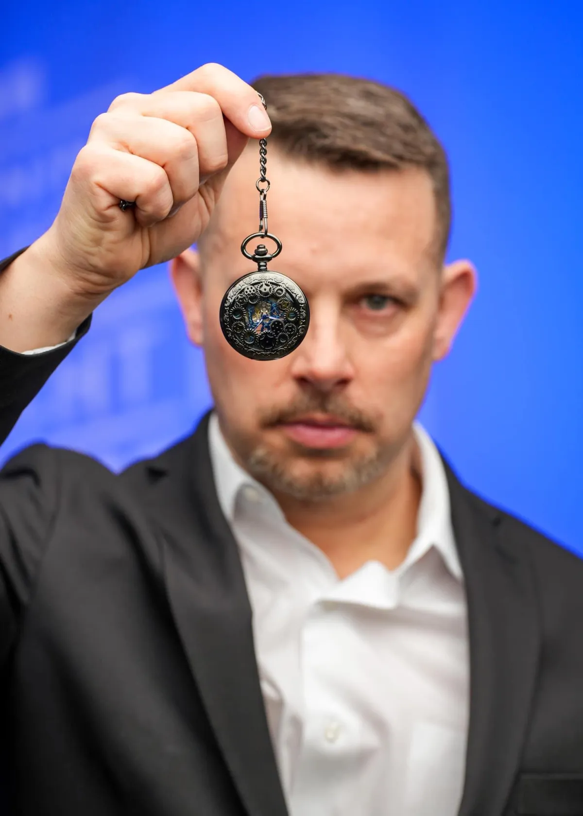 Joe Hussey, The Hypnotic Jester, holding a pocket watch as gold rings ripple outward