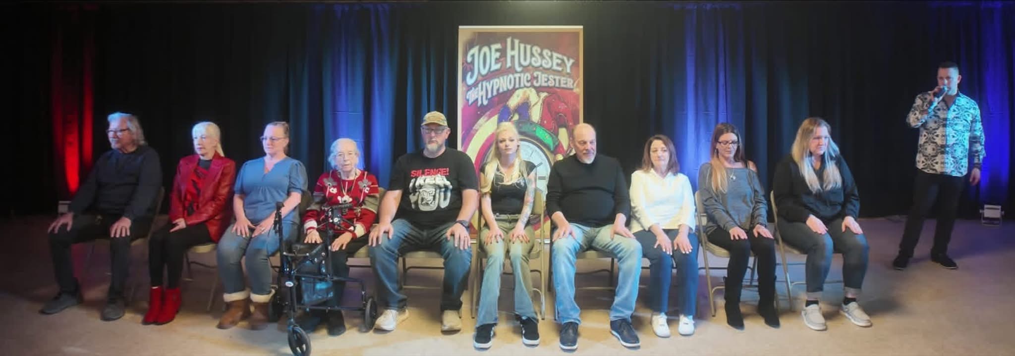 Joe Hussey on stage with a row of volunteers under blue lights